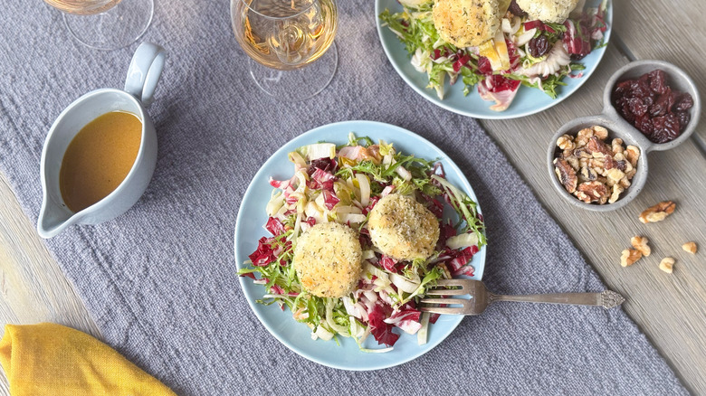 Breaded and baked goat cheese salad with dressing, walnuts, and dried cherries on table