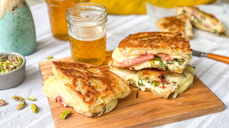 Grilled Italian picnic sandwiches on cutting board with beer and pistachios
