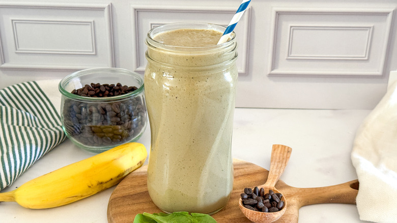 Coffee protein smoothie next to banana, coffee beans, and spinach