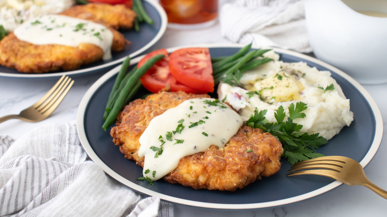 Chicken fried chicken on plate with gravy, mashed potatoes, and vegetables