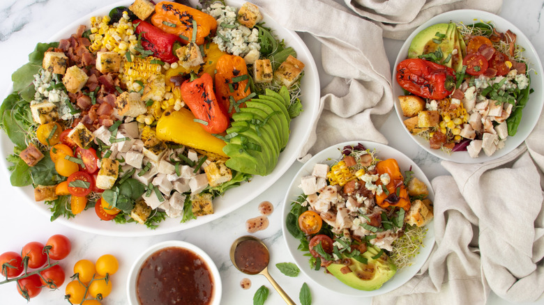 rotisserie chicken salad loaded with veggies, bacon, and raspberry dressing on a platter and small plates