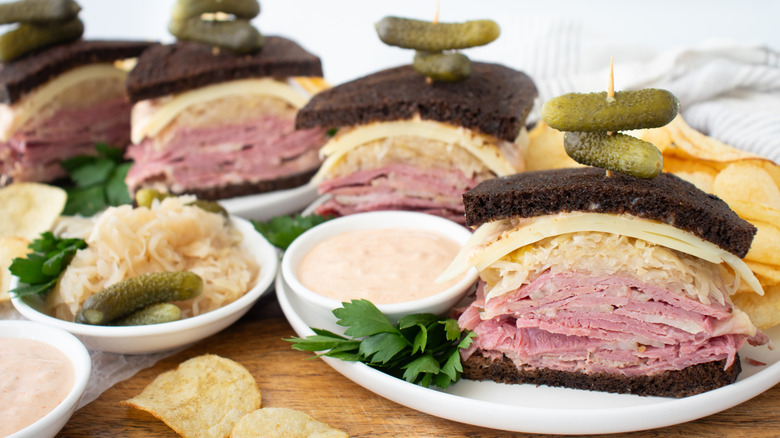 close up of halved reuben sandwiches stacked on plates with pickles on top