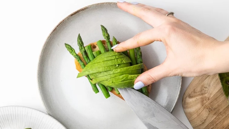 Person plating avocado on asparagus toast