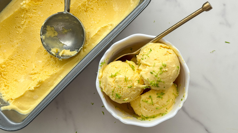 Scoops of mango ice cream in bowl next to loaf pan with ice cream