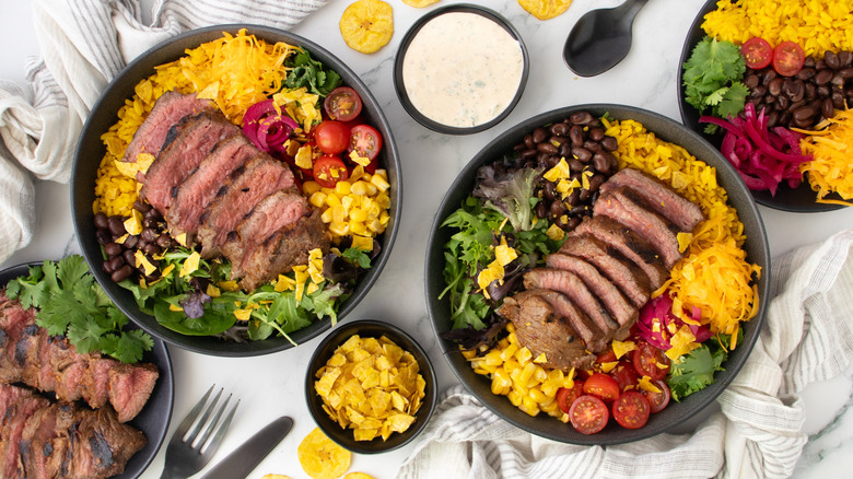 Steak taco bowls next to bowl of ranch and plate with various toppings