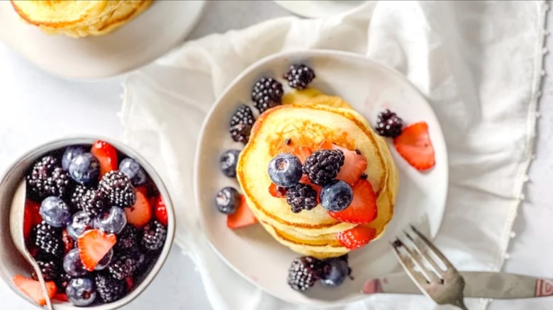White plate with fluffy lemon ricotta pancakes garnished with macerated berries