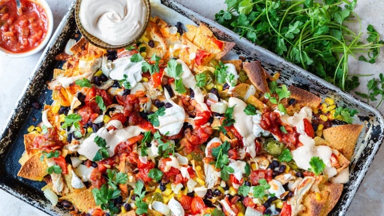 Chicken nachos in a baking tray with sour cream and salsa on the side