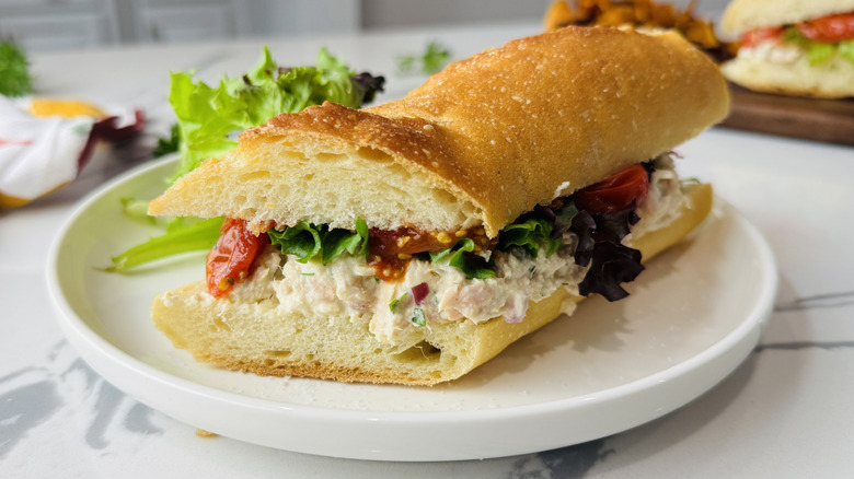 Tuna salad sandwich on a white plate with greens on the side