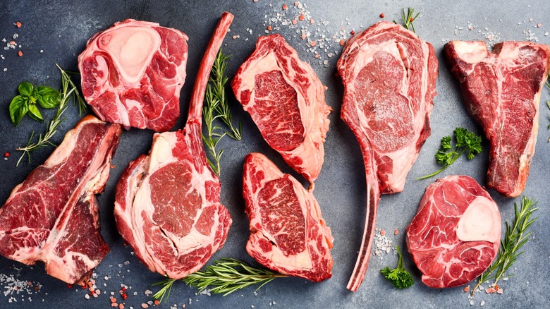 Cuts of raw bone-in steak laid out on a grilltop with sprigs of rosemary and pinches of salt.